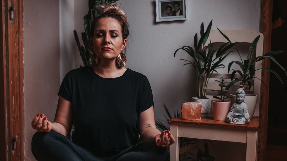 Peaceful female in black clothes and stylish earring meditating during yoga session at home